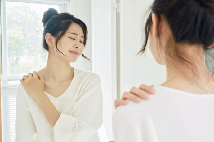肩に手をあてて鏡の前に立つ女性