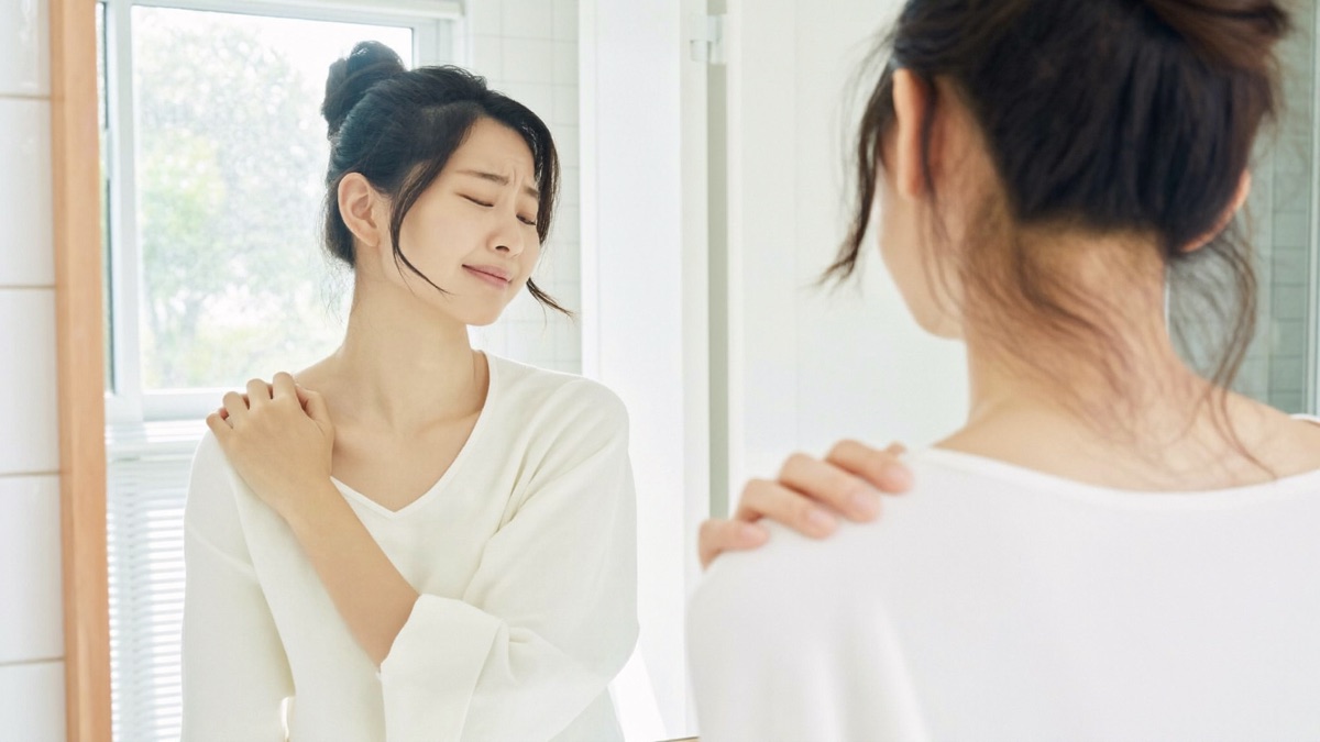 肩に手をあてて鏡の前に立つ女性